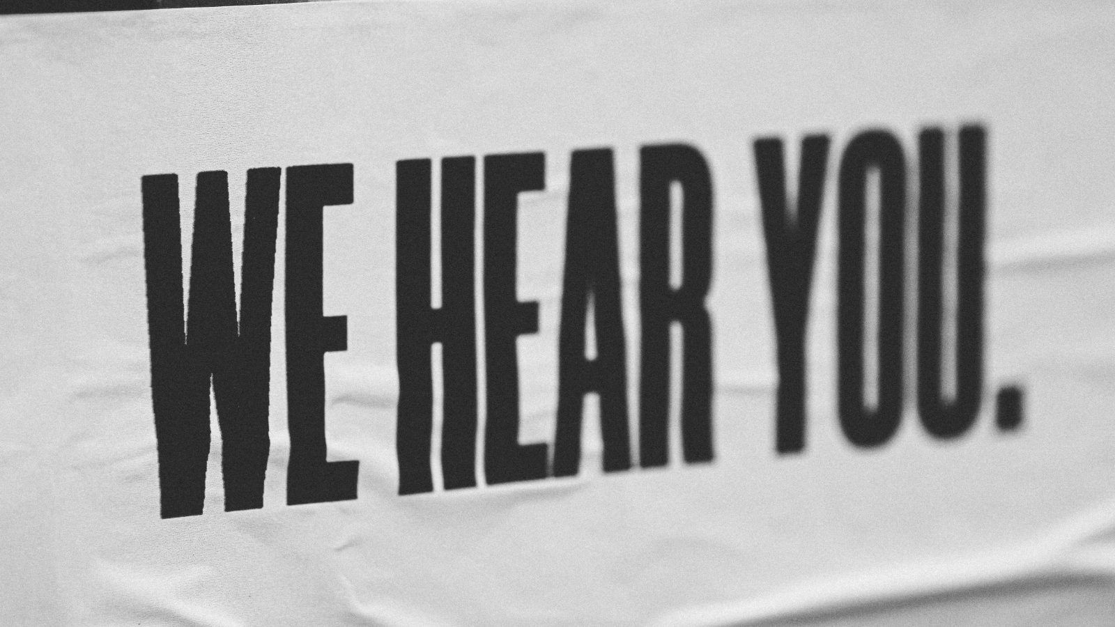 We Hear You written in black over a white background cloth banner